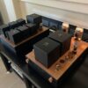 A GM70 Integrated Amplifier setup on a wooden desk featuring glowing tubes and several black electronic boxes with white symbols, perfect for any audiophile. A GM70 Integrated Amplifier setup on a wooden desk featuring glowing tubes and several black electronic boxes with white symbols, perfect for any audiophile.