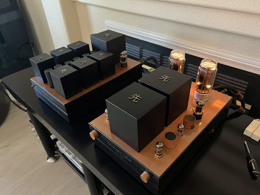 A GM70 Integrated Amplifier setup on a wooden desk featuring glowing tubes and several black electronic boxes with white symbols, perfect for any audiophile. A GM70 Integrated Amplifier setup on a wooden desk featuring glowing tubes and several black electronic boxes with white symbols, perfect for any audiophile.