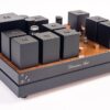 High-end tube amplifier with multiple black transformer covers and a wooden base, featuring The Phono Stage branding and visible tubes. High-end tube amplifier with multiple black transformer covers and a wooden base, featuring The Phono Stage branding and visible tubes.