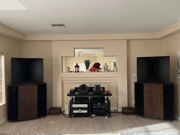 A living room showcases Vista 3-Way Horn Speakers flanking the fireplace, with a shelving unit for audio gear. The mantel is adorned with vases and red flowers. A living room showcases Vista 3-Way Horn Speakers flanking the fireplace, with a shelving unit for audio gear. The mantel is adorned with vases and red flowers.