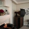 A Vista 3-Way Horn Speaker with a vintage flair stands by the wall adorned with a rose painting. Nearby, electronic audio components are placed on a stand alongside decorative items on the mantel. A Vista 3-Way Horn Speaker with a vintage flair stands by the wall adorned with a rose painting. Nearby, electronic audio components are placed on a stand alongside decorative items on the mantel.