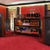 A high-end audio room with large Vista 3-Way Horn Speakers, an amplifier rack with various audio components including a preamplifier, and stone accent walls.