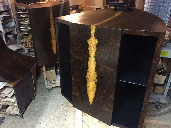 A hexagonal wooden cabinet with an intricate resin inlay on its side, designed to house a Vista 3-Way Horn Speakers, situated in a workshop. A hexagonal wooden cabinet with an intricate resin inlay on its side, designed to house a Vista 3-Way Horn Speakers, situated in a workshop.
